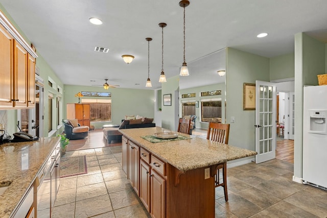 kitchen with white refrigerator with ice dispenser, visible vents, open floor plan, hanging light fixtures, and a kitchen bar