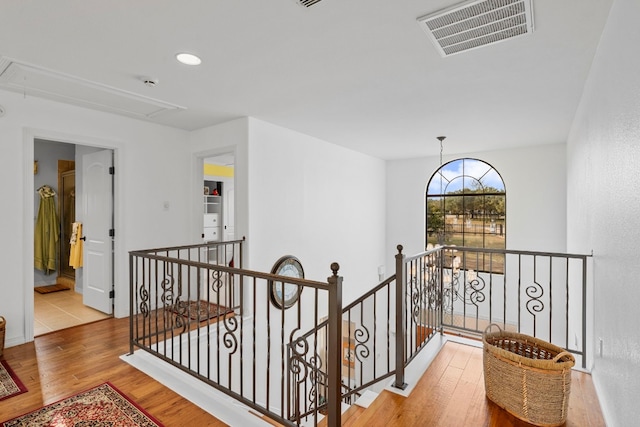 hallway with attic access, visible vents, wood finished floors, and an upstairs landing