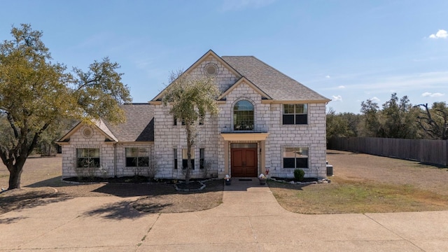 french provincial home featuring stone siding, a shingled roof, and fence