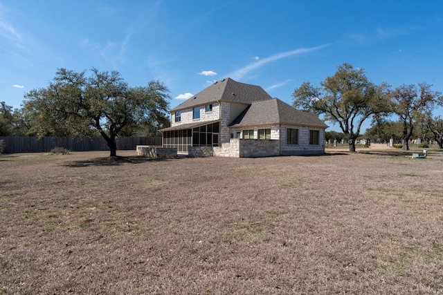 rear view of house with a yard, stone siding, fence, and a sunroom