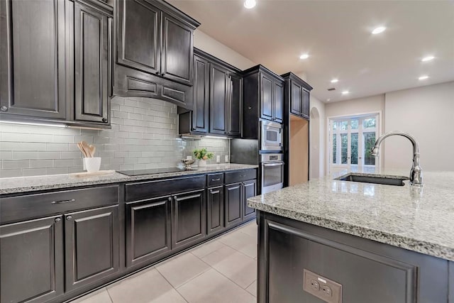 kitchen with light tile patterned flooring, sink, light stone counters, stainless steel appliances, and backsplash