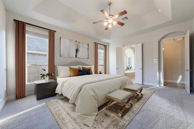 carpeted bedroom featuring ceiling fan, connected bathroom, a raised ceiling, and multiple windows