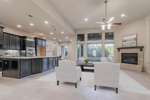 living room with light tile patterned flooring, ceiling fan, and a stone fireplace