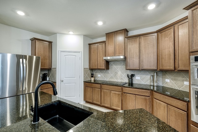 kitchen featuring tasteful backsplash, stainless steel refrigerator, dark stone counters, and sink