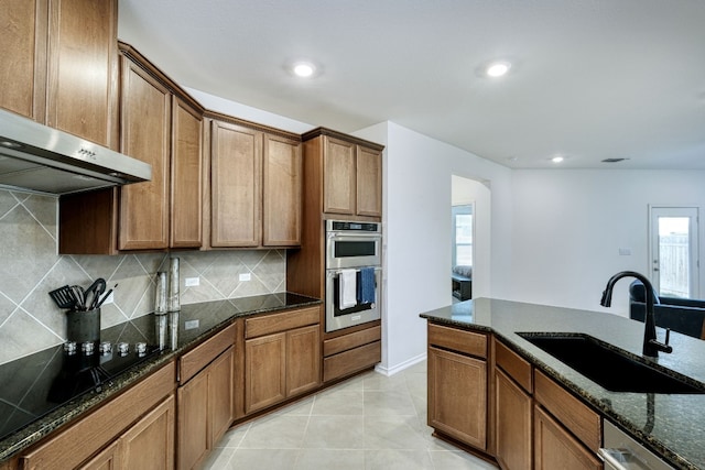 kitchen with sink, stainless steel appliances, tasteful backsplash, dark stone counters, and light tile patterned floors