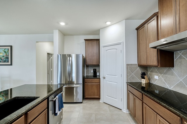 kitchen featuring stainless steel appliances, tasteful backsplash, dark stone counters, extractor fan, and light tile patterned floors