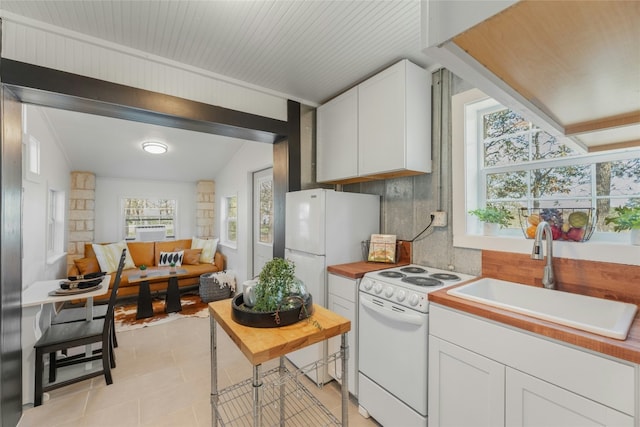 kitchen featuring white appliances, vaulted ceiling, sink, light tile patterned floors, and white cabinetry