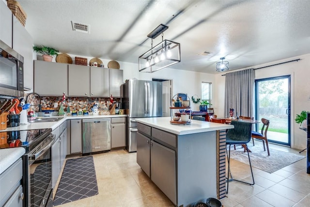 kitchen featuring decorative backsplash, stainless steel appliances, sink, decorative light fixtures, and a center island