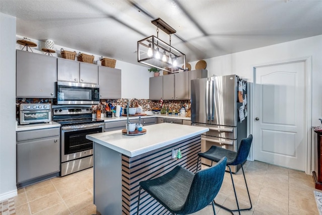 kitchen featuring tasteful backsplash, gray cabinetry, stainless steel appliances, pendant lighting, and a center island