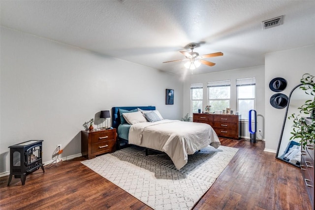 bedroom featuring a textured ceiling, dark hardwood / wood-style flooring, a wood stove, and ceiling fan