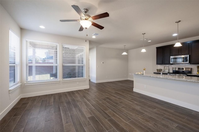 kitchen with ceiling fan, hanging light fixtures, stainless steel appliances, light stone counters, and dark hardwood / wood-style flooring