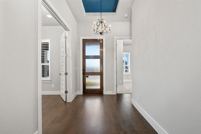 entryway with a notable chandelier, a raised ceiling, dark wood-type flooring, and baseboards