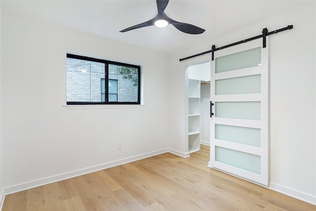 unfurnished bedroom with a walk in closet, ceiling fan, light hardwood / wood-style floors, a barn door, and a closet