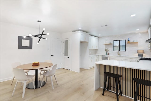 kitchen featuring white cabinetry, light wood-type flooring, stainless steel dishwasher, pendant lighting, and backsplash