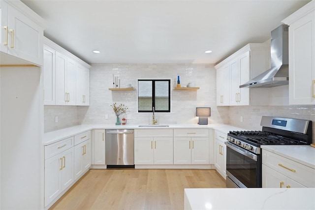 kitchen featuring sink, white cabinets, stainless steel appliances, light wood-type flooring, and wall chimney exhaust hood