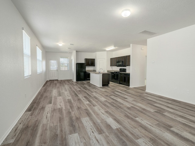 kitchen with sink, dark brown cabinets, a kitchen island, light hardwood / wood-style floors, and black appliances