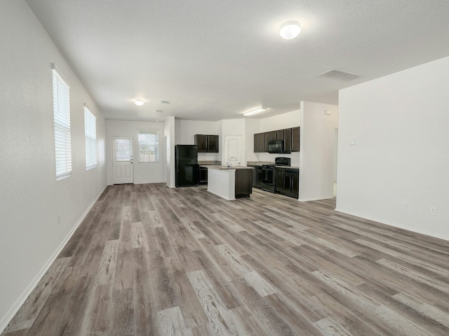 kitchen featuring sink, light wood-type flooring, black appliances, a center island with sink, and a textured ceiling