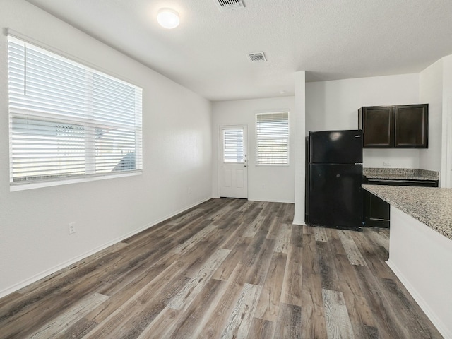 kitchen with dark brown cabinets, a textured ceiling, black refrigerator, dark hardwood / wood-style floors, and light stone countertops