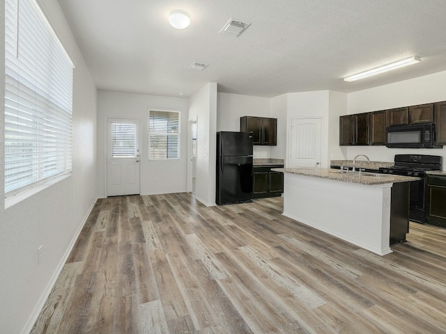 kitchen featuring dark brown cabinets, light hardwood / wood-style flooring, a center island with sink, and black appliances