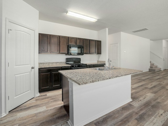 kitchen featuring hardwood / wood-style flooring, sink, a center island with sink, and black appliances