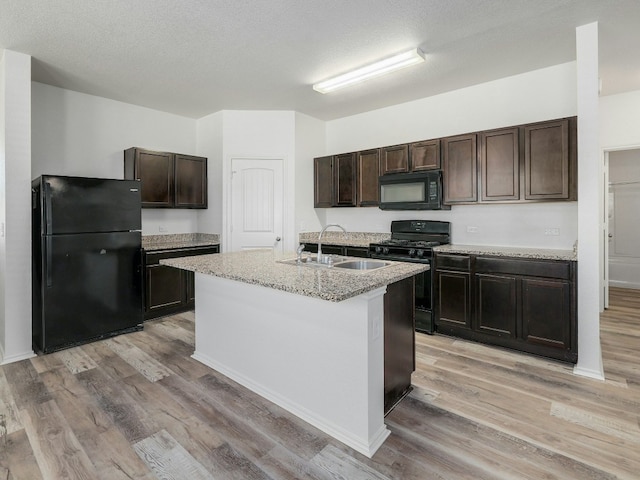 kitchen featuring light wood-type flooring, a kitchen island with sink, dark brown cabinetry, and black appliances