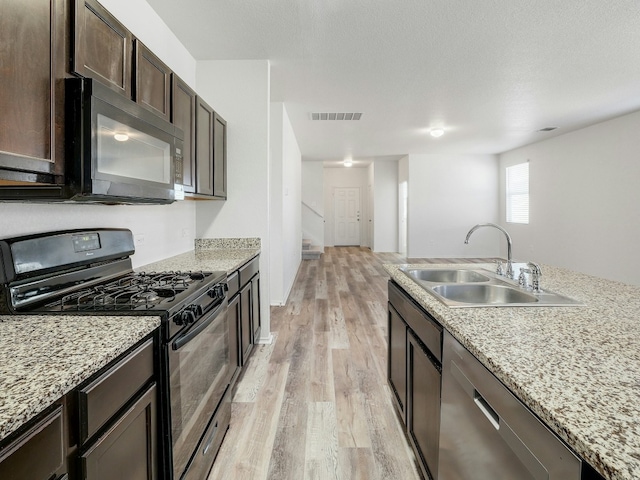 kitchen with light stone counters, dark brown cabinetry, sink, and black appliances