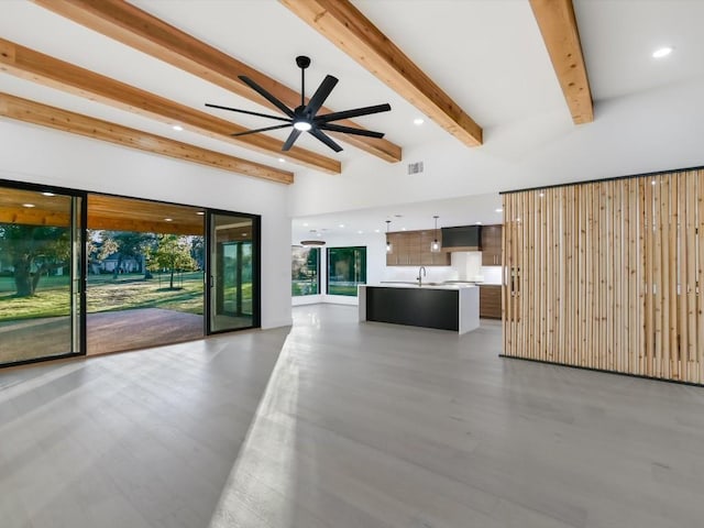 unfurnished living room featuring beam ceiling, ceiling fan, and sink