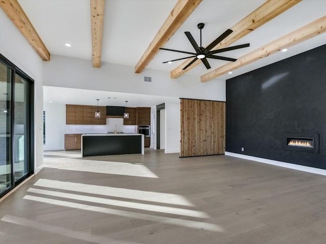 unfurnished living room featuring light wood-type flooring, ceiling fan, sink, beam ceiling, and a fireplace