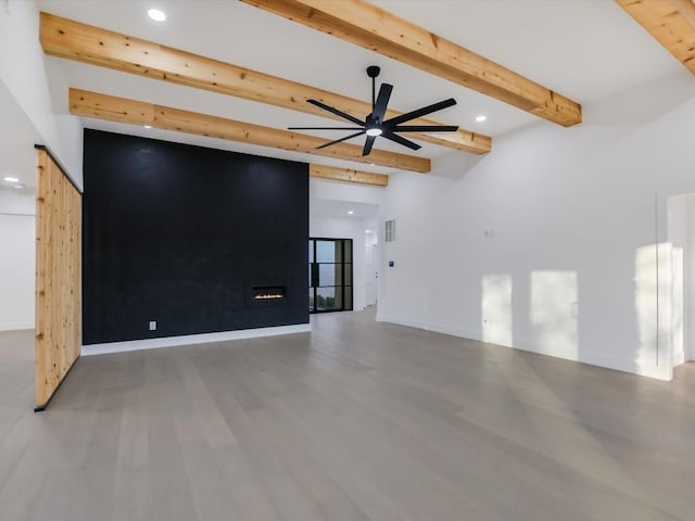 unfurnished room featuring beamed ceiling, ceiling fan, a fireplace, and hardwood / wood-style floors