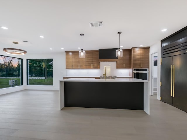 kitchen featuring a kitchen island with sink, sink, hanging light fixtures, light hardwood / wood-style flooring, and stainless steel appliances