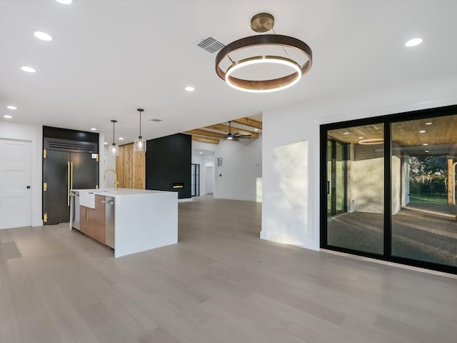 kitchen featuring stainless steel appliances, a kitchen island with sink, ceiling fan, pendant lighting, and beamed ceiling