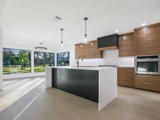 kitchen featuring pendant lighting, a kitchen island with sink, premium range hood, sink, and appliances with stainless steel finishes