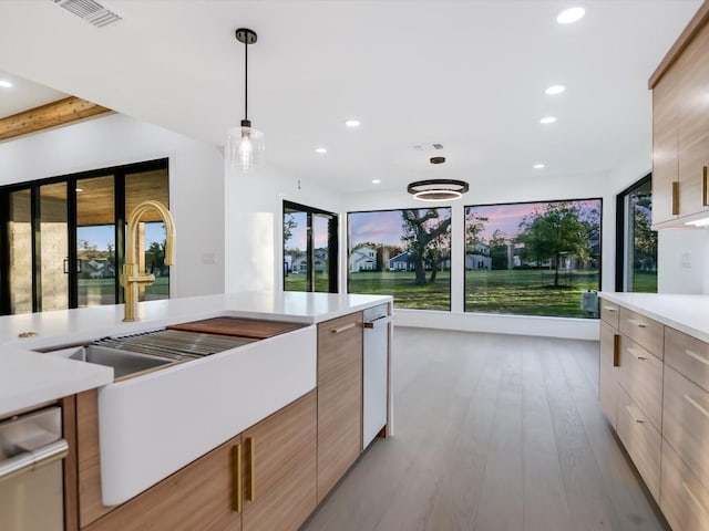 kitchen with sink, light brown cabinets, light hardwood / wood-style flooring, stainless steel dishwasher, and decorative light fixtures