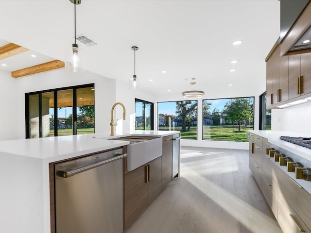 kitchen with beamed ceiling, light hardwood / wood-style floors, decorative light fixtures, a center island with sink, and appliances with stainless steel finishes