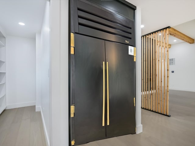 interior space with beam ceiling, stainless steel built in fridge, and hardwood / wood-style floors