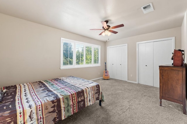 bedroom with ceiling fan, light colored carpet, and two closets