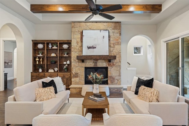 living room featuring beam ceiling, ceiling fan, a fireplace, and light wood-type flooring