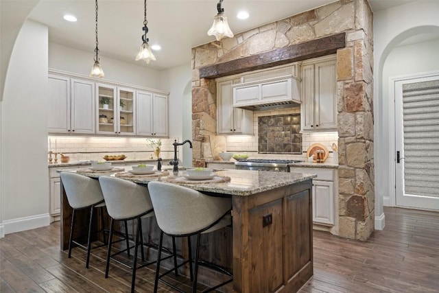 kitchen featuring backsplash, a center island with sink, white cabinets, light stone counters, and dark hardwood / wood-style flooring