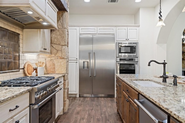 kitchen with premium range hood, dark wood-type flooring, sink, built in appliances, and white cabinetry