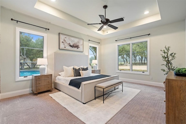 bedroom featuring ceiling fan, light carpet, a tray ceiling, and multiple windows