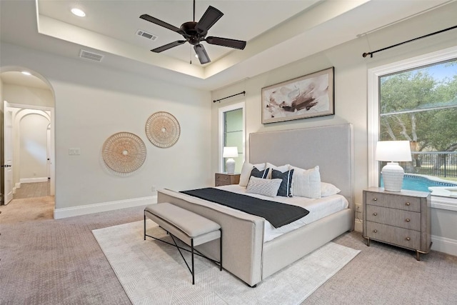 bedroom with light colored carpet, ceiling fan, and a tray ceiling