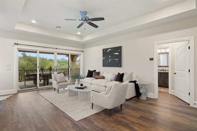 living room featuring a raised ceiling, ceiling fan, and dark wood-type flooring