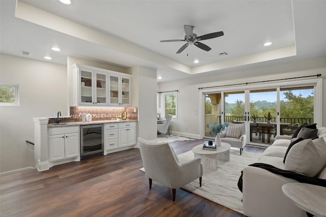 living room with dark hardwood / wood-style flooring, a tray ceiling, beverage cooler, and ceiling fan