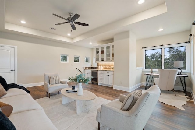 living room featuring a tray ceiling, wine cooler, ceiling fan, and light hardwood / wood-style floors