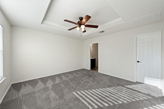 spare room featuring a tray ceiling, ceiling fan, and dark colored carpet