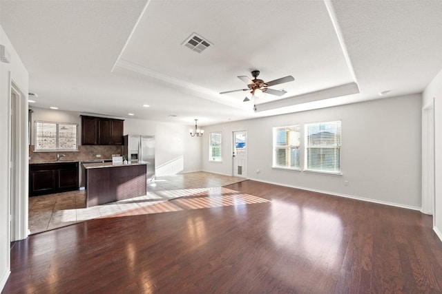 unfurnished living room featuring wood-type flooring, ceiling fan with notable chandelier, and a tray ceiling