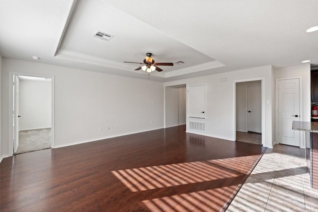 unfurnished living room featuring a raised ceiling, ceiling fan, and dark hardwood / wood-style flooring