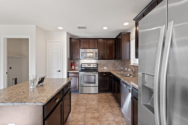 kitchen with a center island, stainless steel appliances, light stone counters, and sink