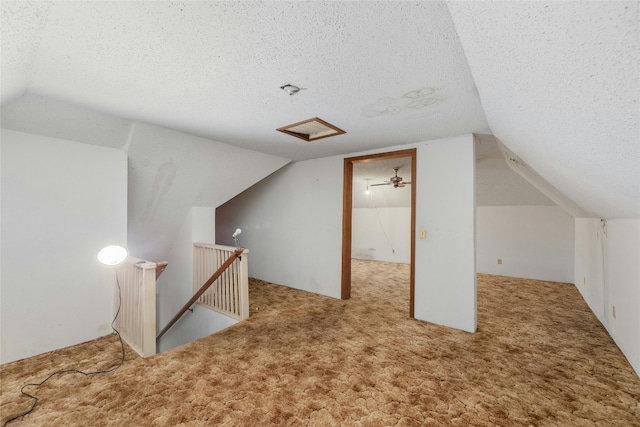 additional living space featuring a textured ceiling, vaulted ceiling, attic access, and light colored carpet