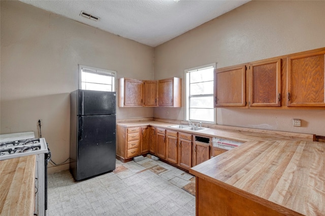 kitchen featuring visible vents, butcher block counters, freestanding refrigerator, white gas range, and a wealth of natural light